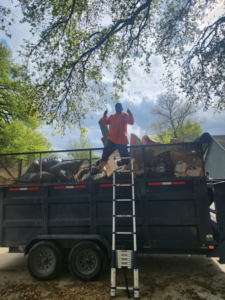 A McMillian Junk Removal worker giving a thumbs-up on top of a full junk removal trailer in Houston, TX
