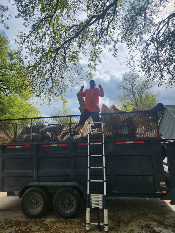 A McMillian Junk Removal worker giving a thumbs-up on top of a full junk removal trailer in Houston, TX