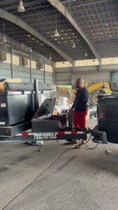 A worker operating the hydraulic mechanism of a dump trailer inside a facility, performing junk removal for Jax Junkies Removal LLC in Jacksonville, FL