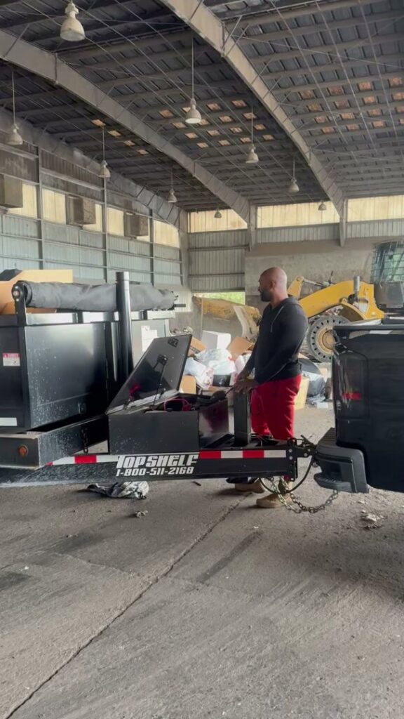 A worker operating the hydraulic mechanism of a dump trailer inside a facility, performing junk removal for Jax Junkies Removal LLC in Jacksonville, FL