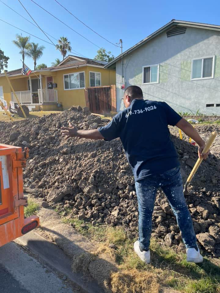 A worker shoveling a large pile of dirt and construction rubble for Dos Muchos Junk Removal LLC in San Diego, CA.