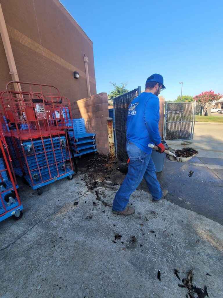 A worker from Haulaway Junk Removal Service, LLC sweeping debris outside a commercial building in Dallas, TX.