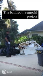 A worker standing next to a pile of bathroom remodel debris and trash bags, showcasing a junk removal service by Jacksonville Hauling & Junk Removal in Jacksonville, FL.