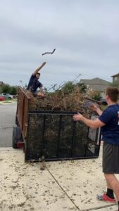 Two Firefighter Junk Removal workers in Austin, TX, loading brush and branches into a junk removal trailer.