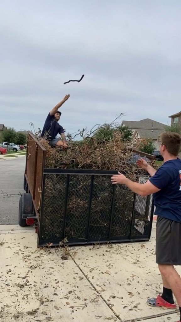 Two Firefighter Junk Removal workers in Austin, TX, loading brush and branches into a junk removal trailer.