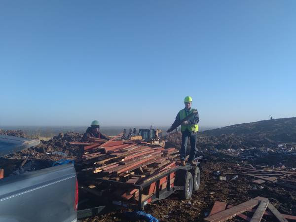 Two workers loading wooden construction debris onto a trailer at a job site for D & Ds Junk Removal Services in Houston, TX