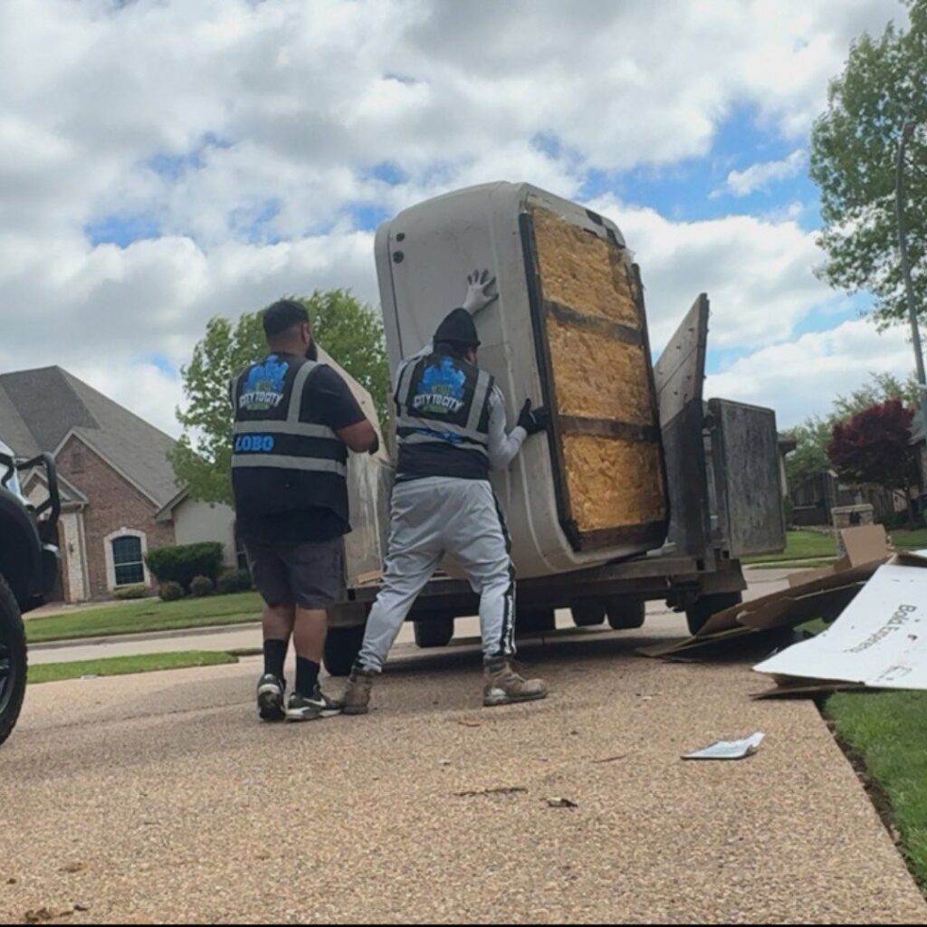 Two City to City Junk Removal workers loading a large hot tub onto a trailer in Fort Worth, TX.