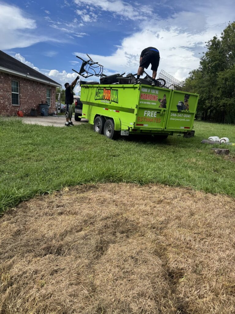 Workers loading various junk items into a bright green Clear Your Junk - Pearland trailer during a removal job in Houston, TX.