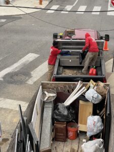 Two workers from Kay's Brothers Junk Removal loading items into a pickup truck, with a full junk trailer in the foreground in Philadelphia, PA.