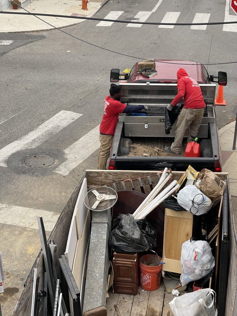 Two workers from Kay's Brothers Junk Removal loading items into a pickup truck, with a full junk trailer in the foreground in Philadelphia, PA.