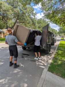 Two workers loading a large sofa into a junk removal trailer for 2 Bald Guys Hauling & Junk Removal in San Antonio, TX.