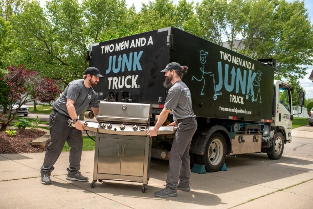 Two workers from Two Men and a Junk Truck removing a large BBQ grill and loading it onto their truck in Columbus, OH.