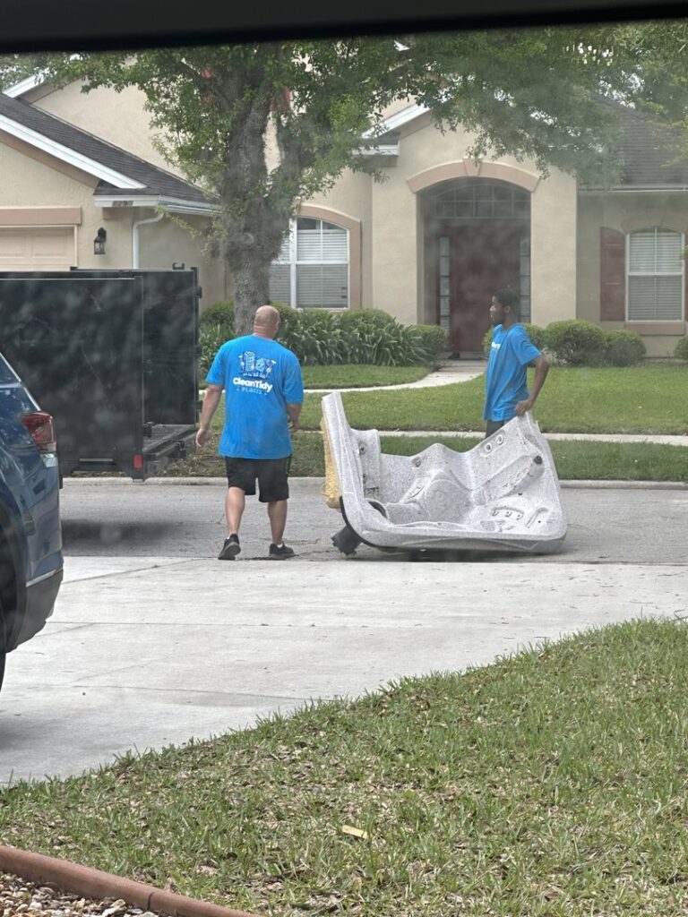 Two workers from Clean Tidy Places in Jacksonville, FL, removing a large hot tub for a professional junk removal service.
