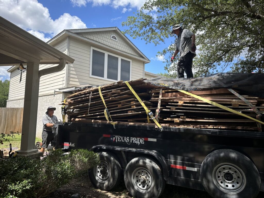 Two workers securing a large load of wood planks on a trailer for 2 Bald Guys Hauling & Junk Removal in San Antonio, TX.