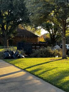 A Hud's Haul Away Junk Removal & Demolition trailer loaded with yard waste and trash bags on a street in Fort Worth, TX.