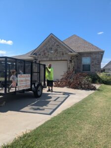 A Herrera Hauling & Junk Removal trailer parked next to a pile of yard waste for removal in Fort Worth, TX.