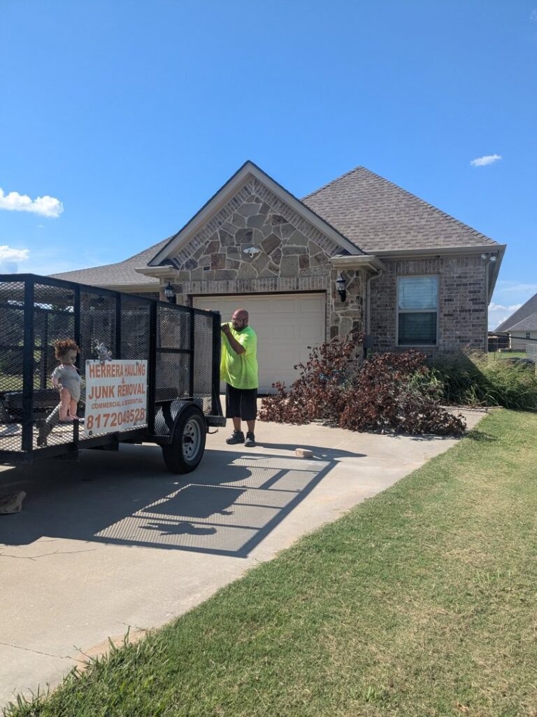 A Herrera Hauling & Junk Removal trailer parked next to a pile of yard waste for removal in Fort Worth, TX.